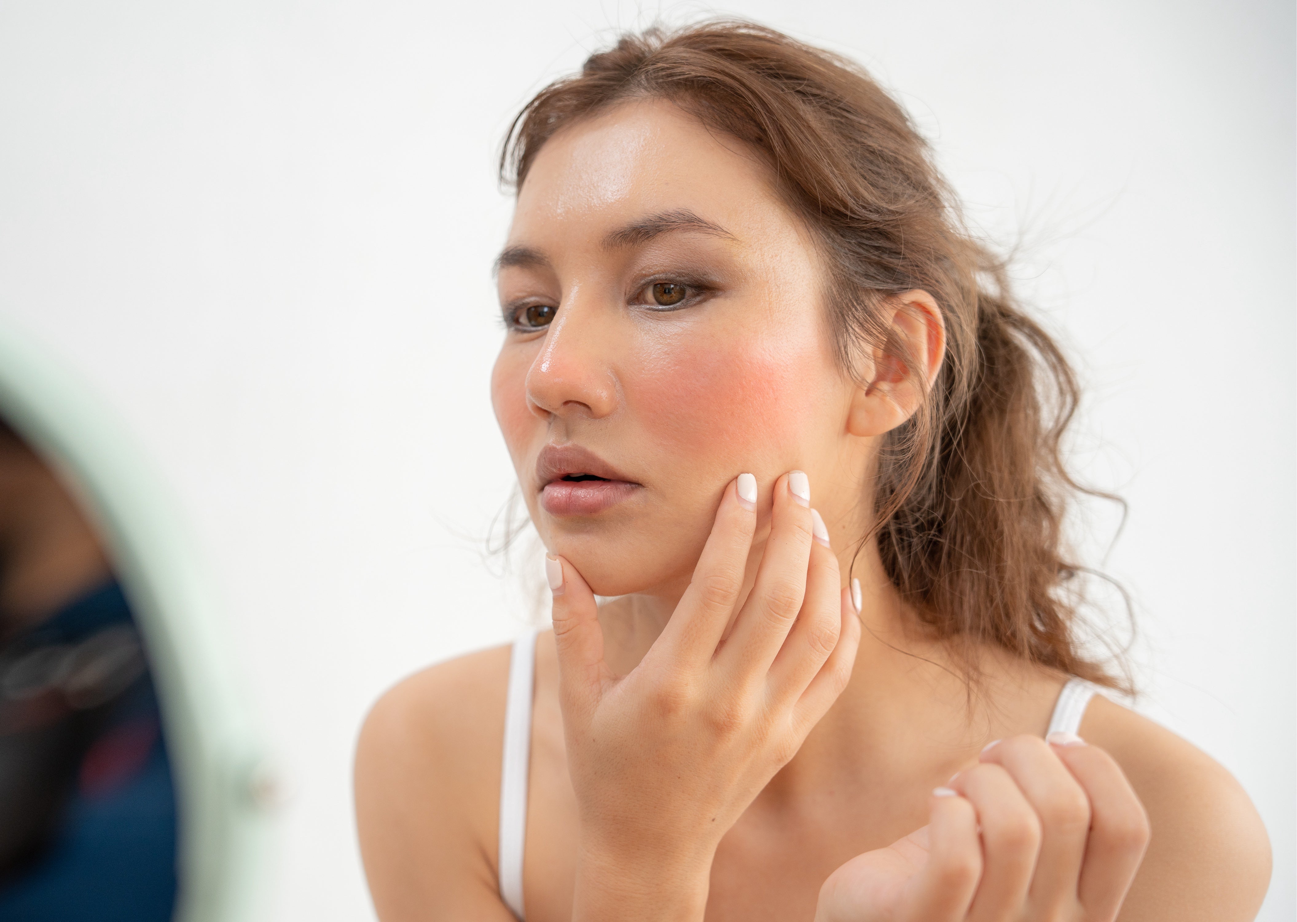 woman looking in mirror critiquing her skin