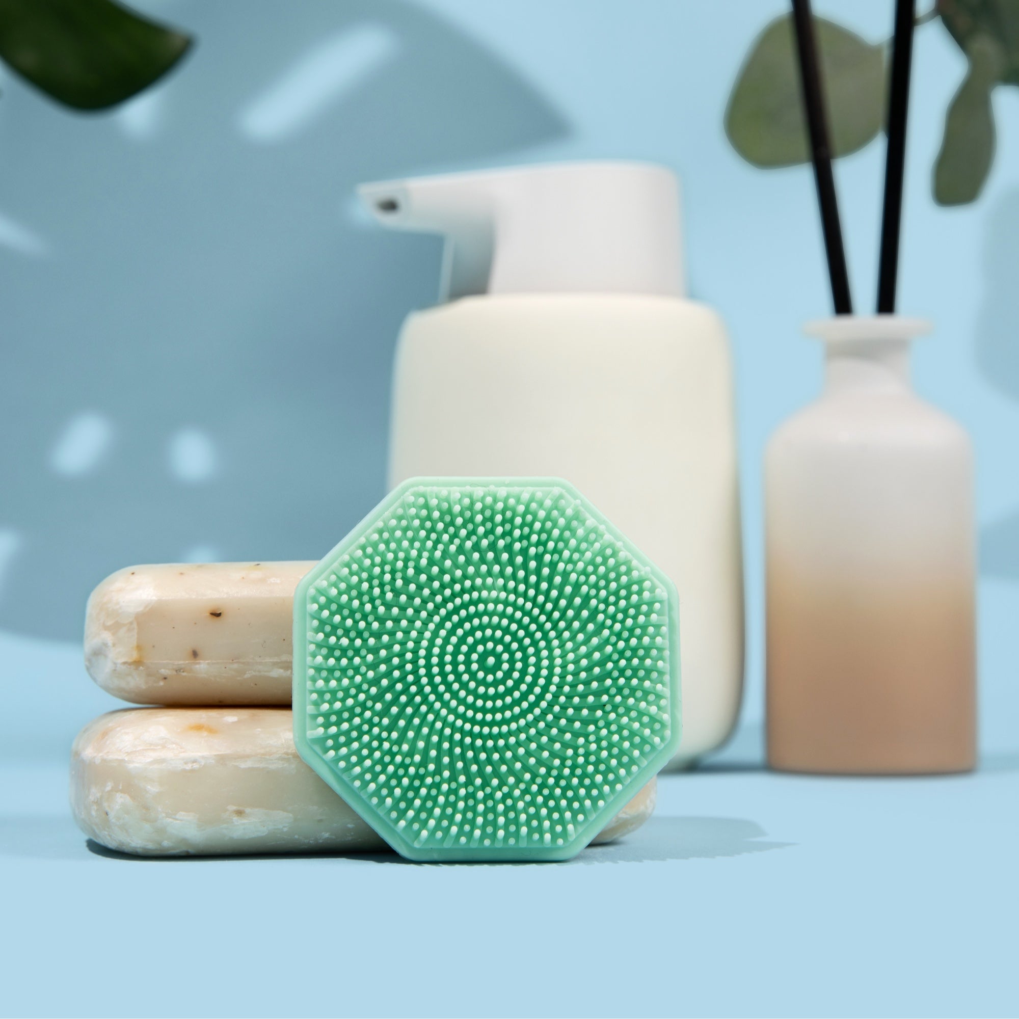 Sud Scrub face scrubber in a bathroom setting leaning against bars of soap, front view