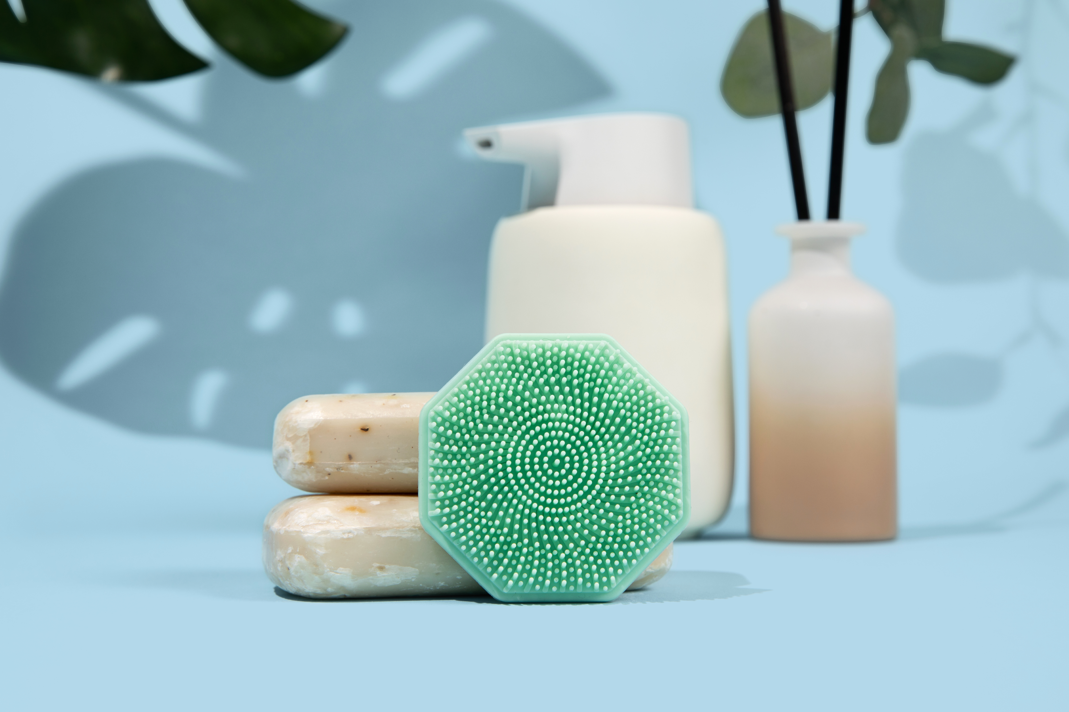 Sud Scrub face scrubber in a bathroom setting leaning against bars of soap, front view