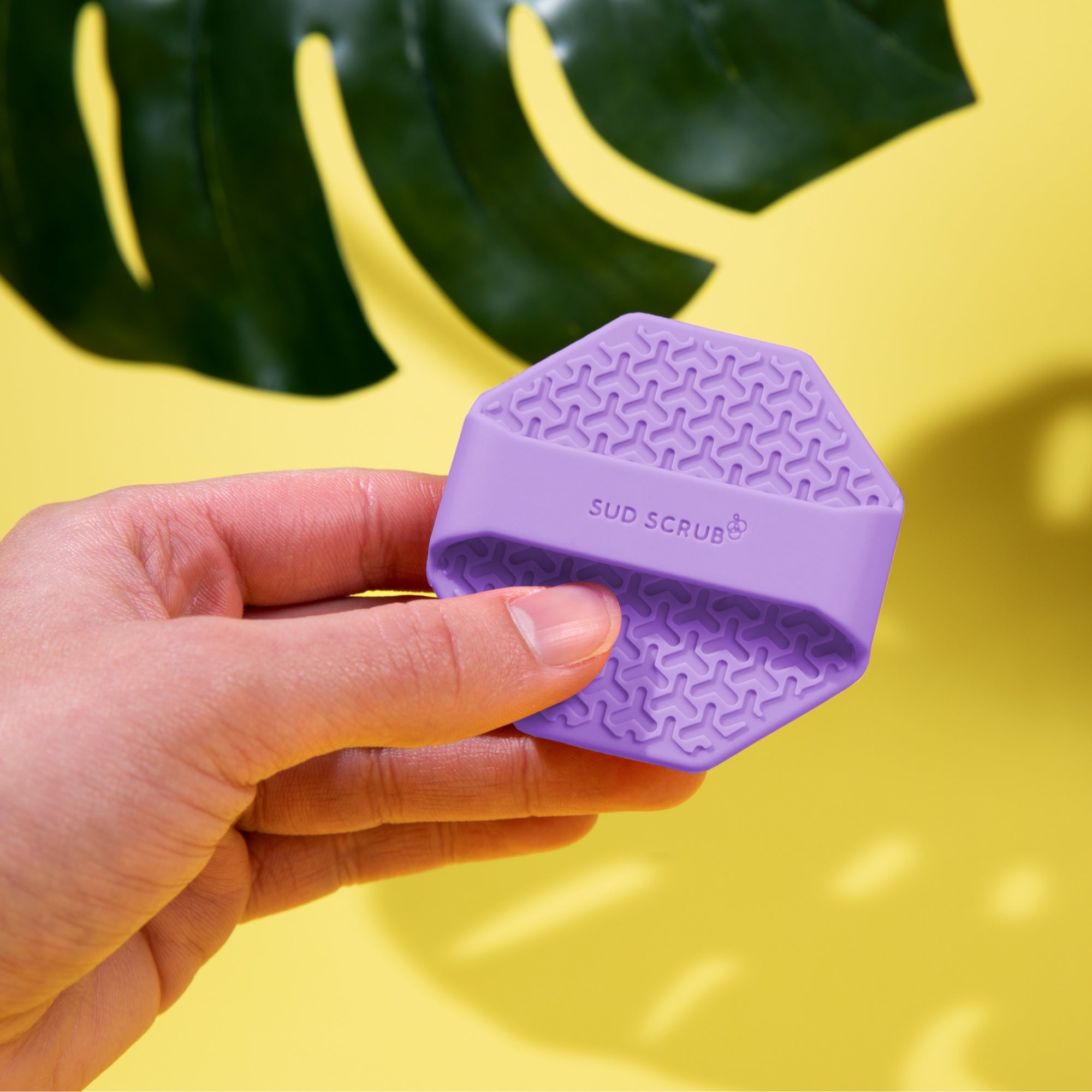 Hand holding sud scrub face scrubber, back view