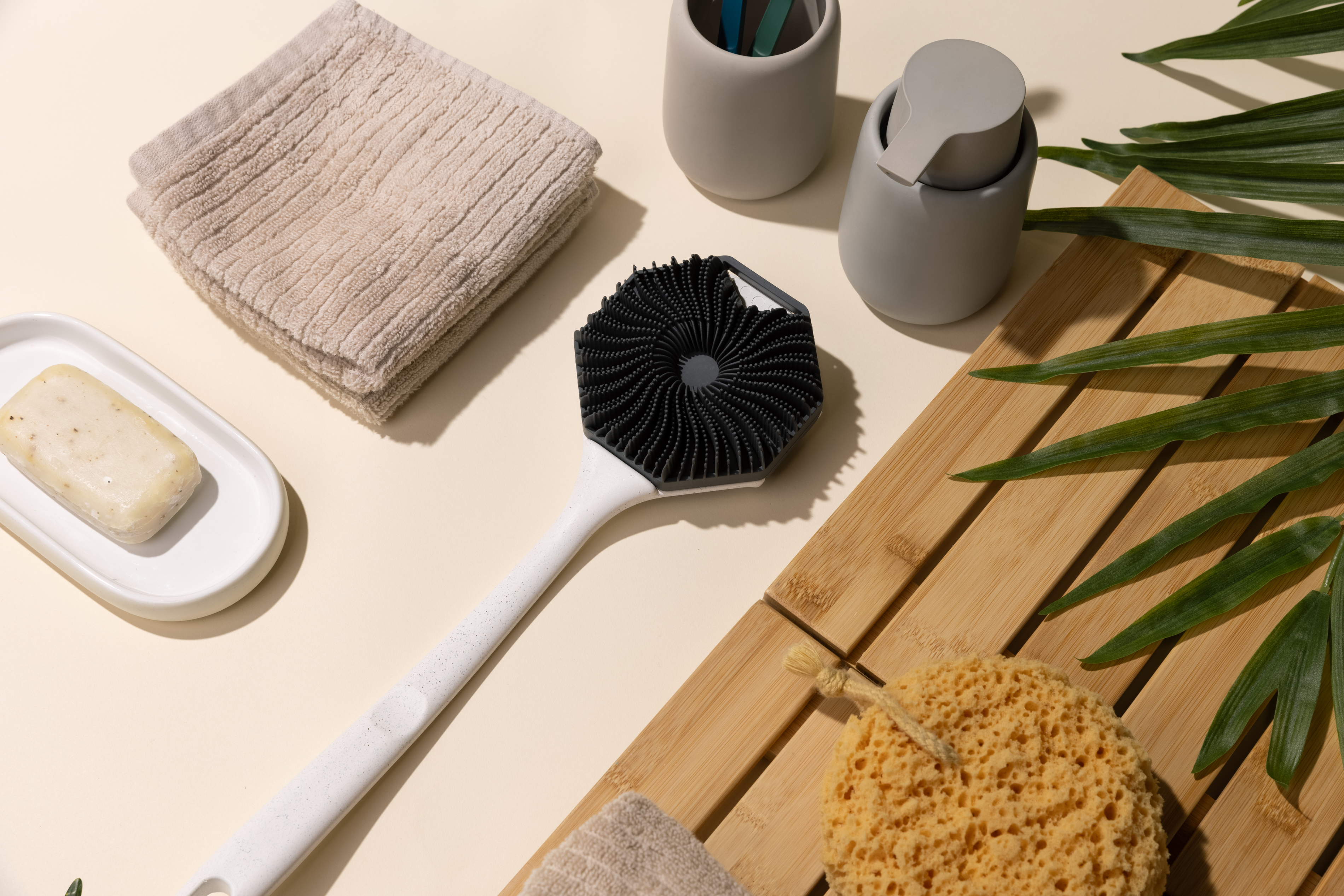 Sud Scrub Body scrubber fastened onto Sud Scrub Extender Handle laying amongst soap and towels in a bathroom setting