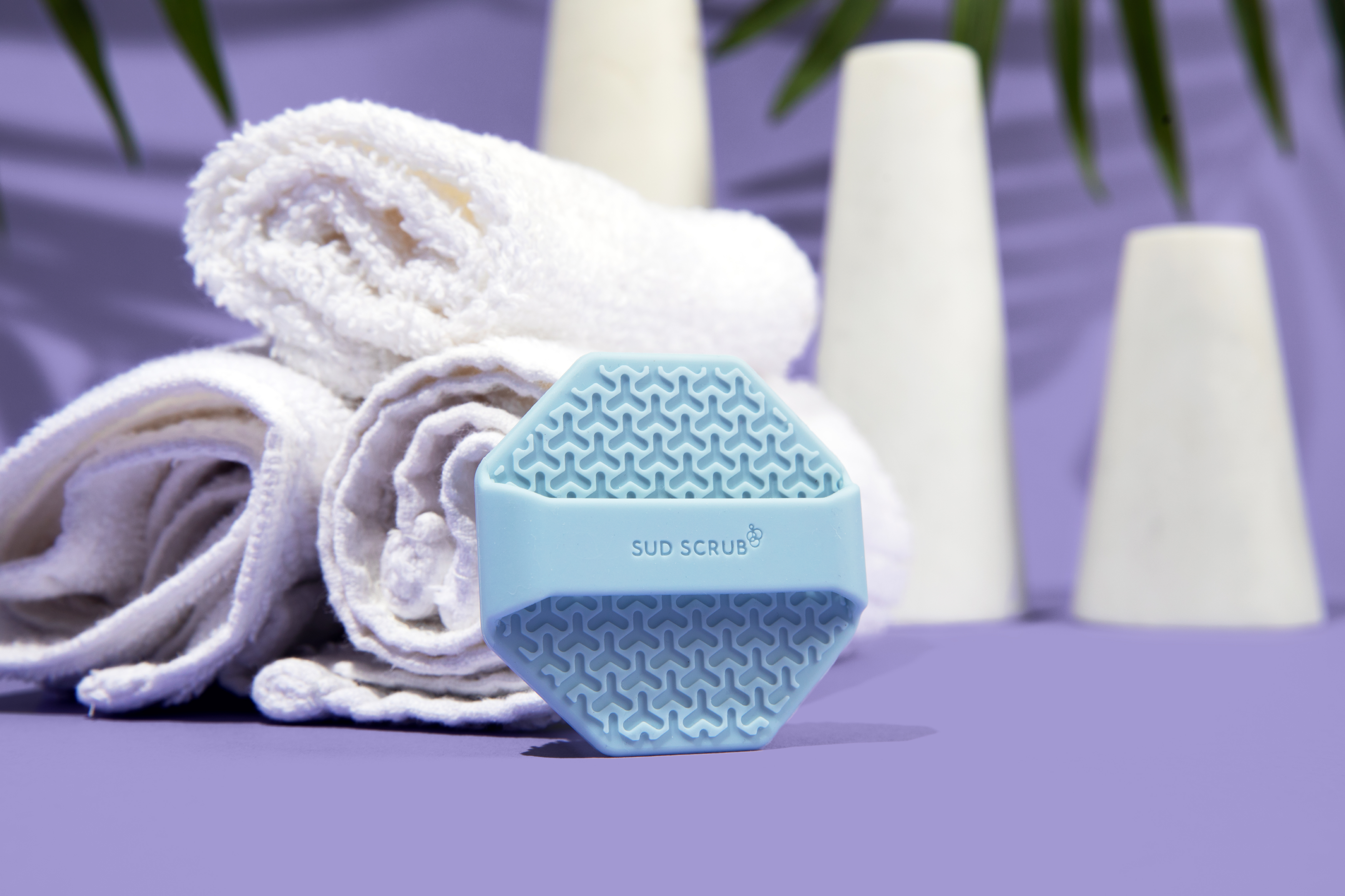 Sud Scrub face scrubber leaning against towels in a bathroom setting
