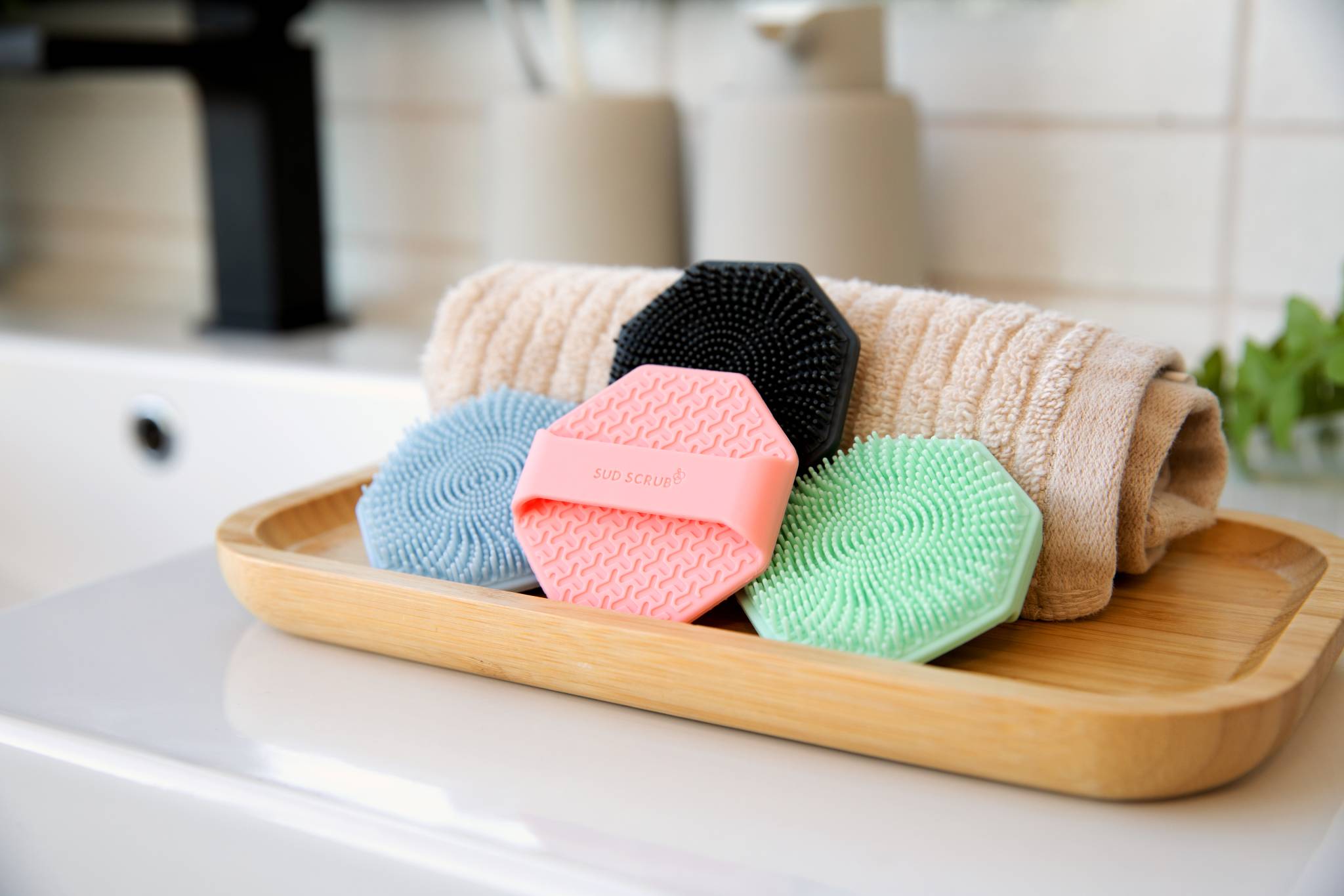 multiple colors of the Sud Scrub face scrubber in a bathroom setting